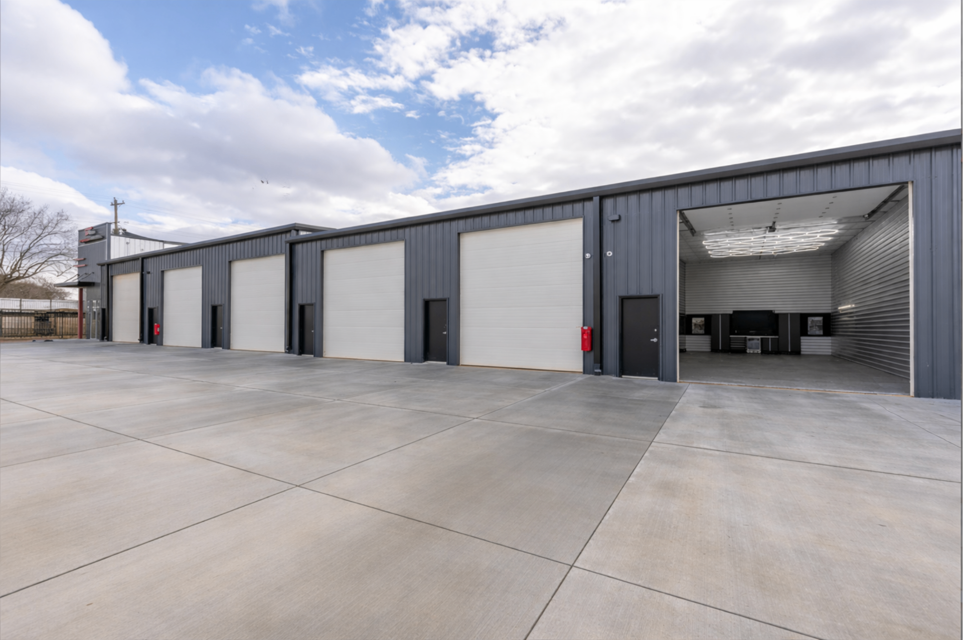 Exterior row of Storage Caves garage condo units with oversized white roll-up doors, open bay revealing finished interior, and wide concrete drive aisle
